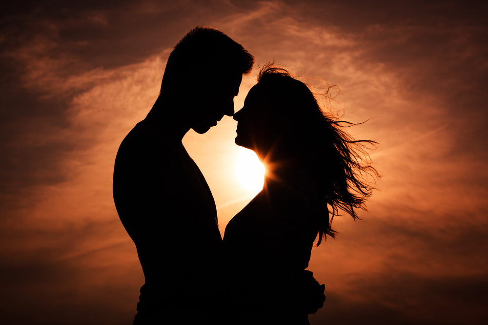 Una pareja mirándose a los ojos muy cerca uno del otro casi besándose frente a la luz del atardecer naranja - El Templo de Gala -Tarot