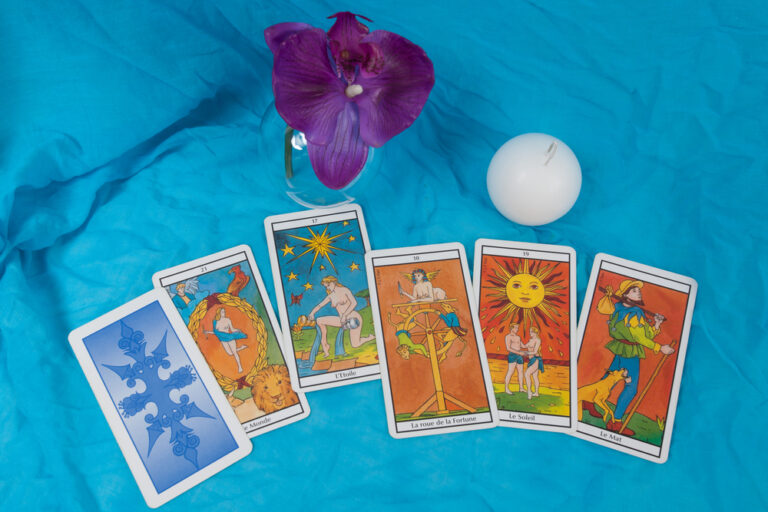 Divination - El templo de Gala - El templo de Gala Cartas de tarot sobre un fondo de tela azul con una orquídea morada en un jarrón de cristal y una bola blanca - El Templo de Gala -Tarot