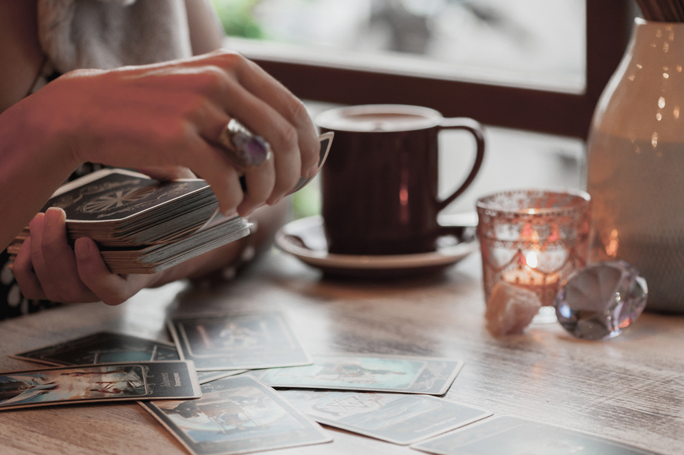 Las manos de una mujer en un entorno hogareño echando las cartas de tarot mientras se toma una taza de café - El Templo de Gala -Tarot