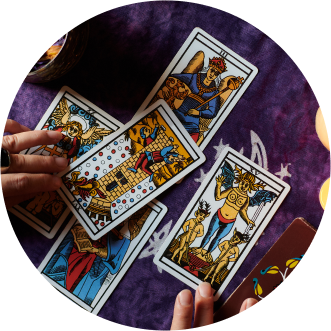 Una imagen recortada circular donde se ven unas manos repartiendo cartas de tarot sobre un fondo de tejido morado con estrellas y lunas dibujadas en color plata - El Templo de Gala -Tarot