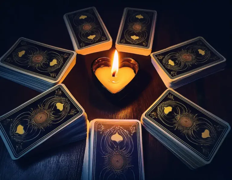 tarot y velas - El templo de Gala - El templo de Gala Montones de cartas repartidos en una mesa al rededor de una vela con forma de corazón que alumbra las cartas de manera ténue | El Templo de Gala | Tarot | Amor